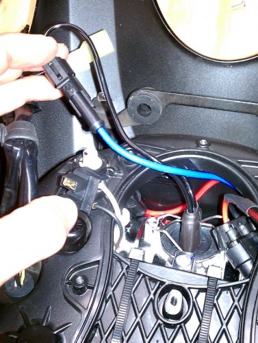 The red wire for the HID bulb is pushed into the top of the headlight bucket.  The blue wire that I'm holding will be next.
